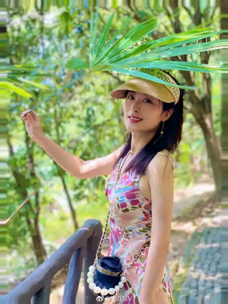 徐百慧穿花色吊带长裙,半扎高马尾,戴卡色遮阳帽,优雅