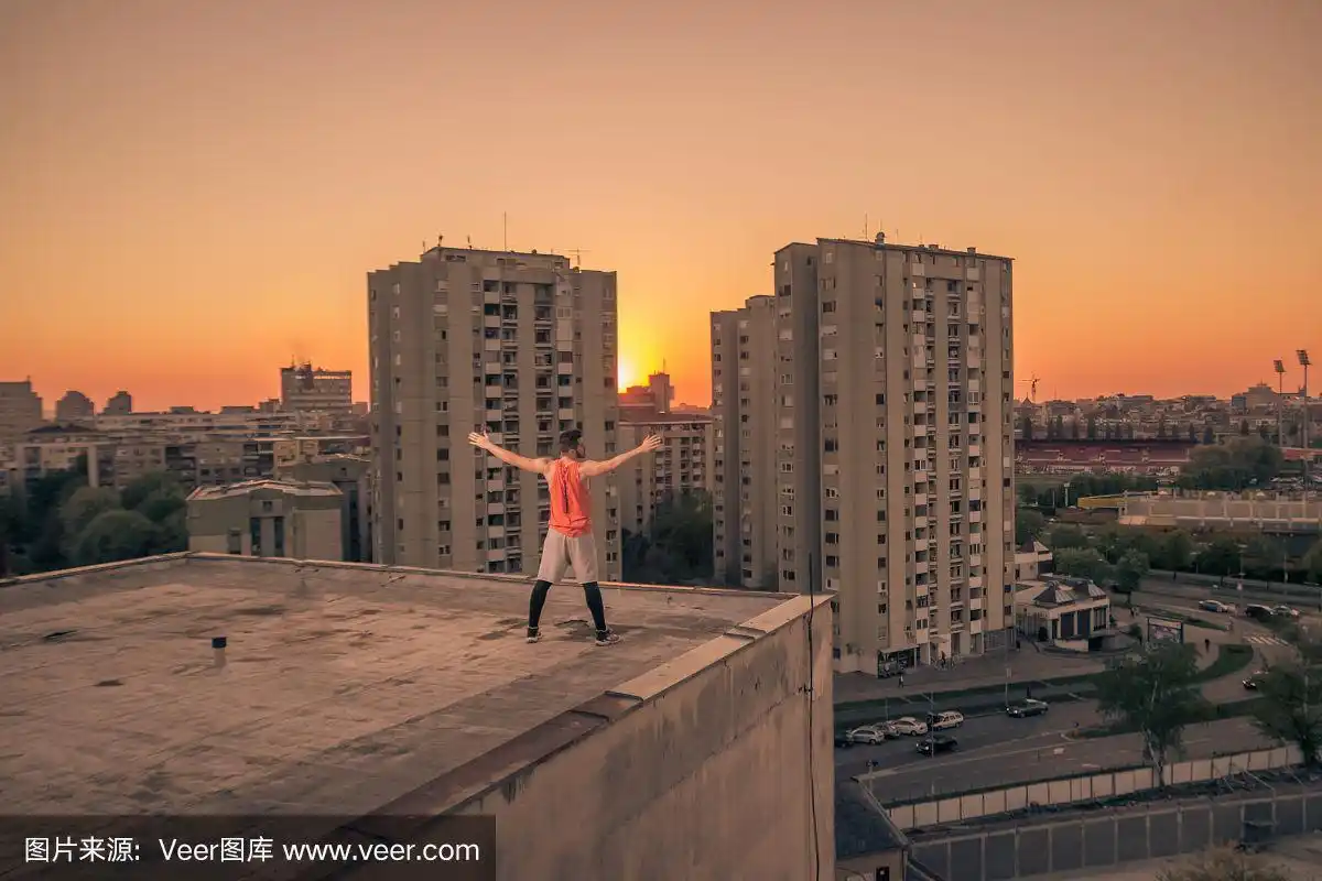 运动员骄傲成功,站在屋顶,伸开双臂,城市城市景象
