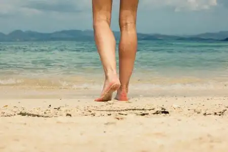 脚和腿的年轻女子在沙滩上行走照片