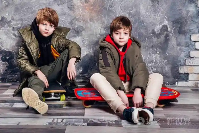 两个穿着休闲服的双胞胎小男孩坐在工作室的滑板上青少年和儿童时尚