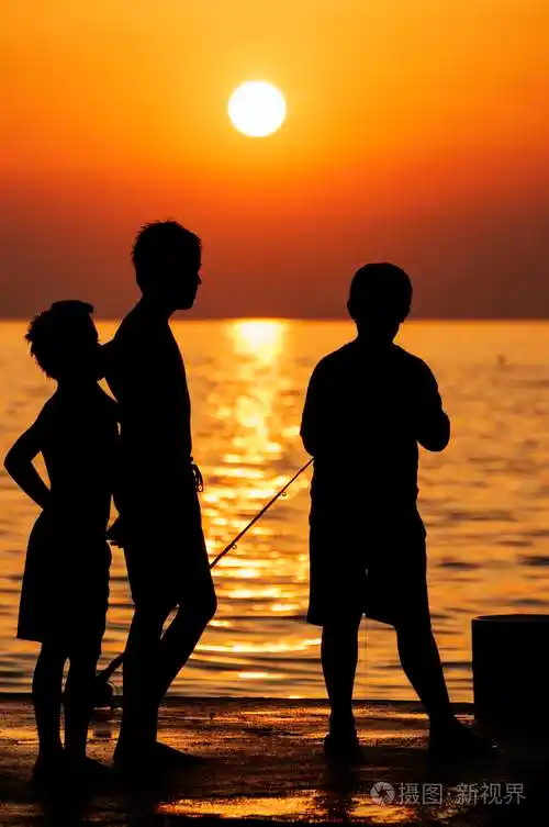 三个男孩在码头日落时钓鱼的剪影金色的大海和夕阳在