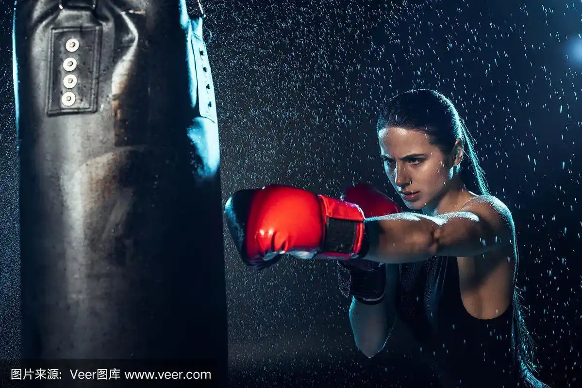 强壮的拳击手在红色拳击手套下训练在黑色水滴