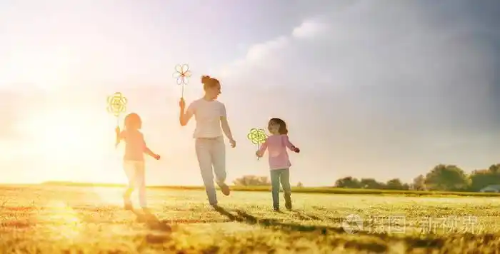 年轻的母亲和两个女儿在日落的背景下在草地上欢笑和玩耍.