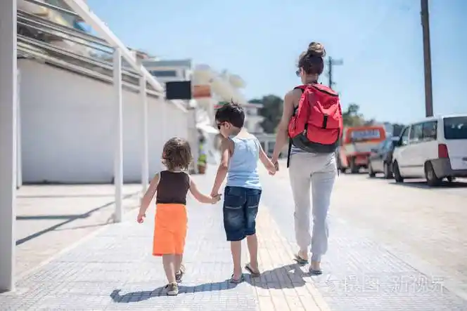 单亲妈妈带着两个孩子走在海滨避暑山庄,在温暖的阳光下,手牵着手从