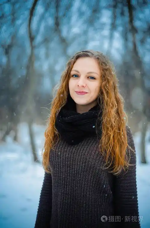 欧洲人的年轻女孩与红色的头发和蓝色的眼睛在自然公园里冬天走在雪上