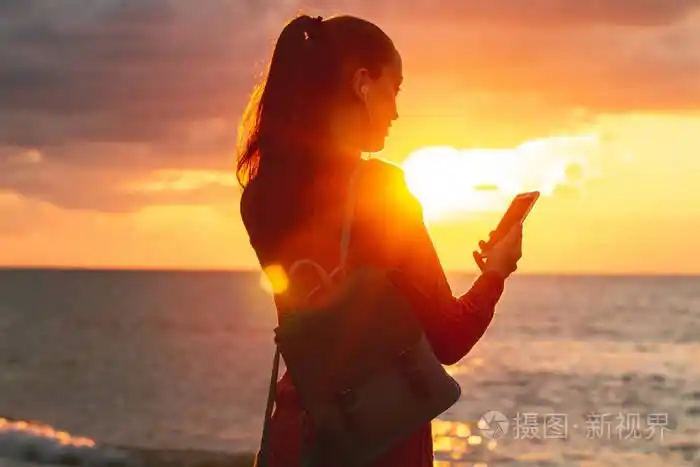 一个年轻快乐的女人在日落时听音乐,在海滩上享受美丽的海景.