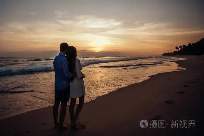 女孩和男孩的后视镜互相拥抱年轻夫妇在海滩上欣赏日落
