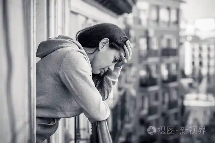黑色和白色的悲伤不堪重负的妇女站在阳台上休息栏杆上的看法照片