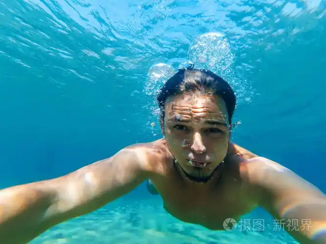 年轻的男性潜水员在海里游泳, 在蓝色的水, 使一个自拍