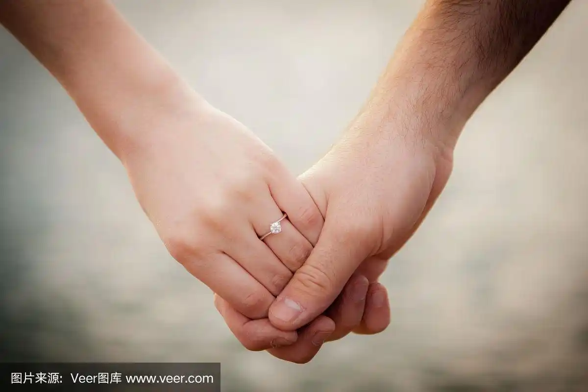 年轻的新婚夫妇手牵着手与一个湖的背景.