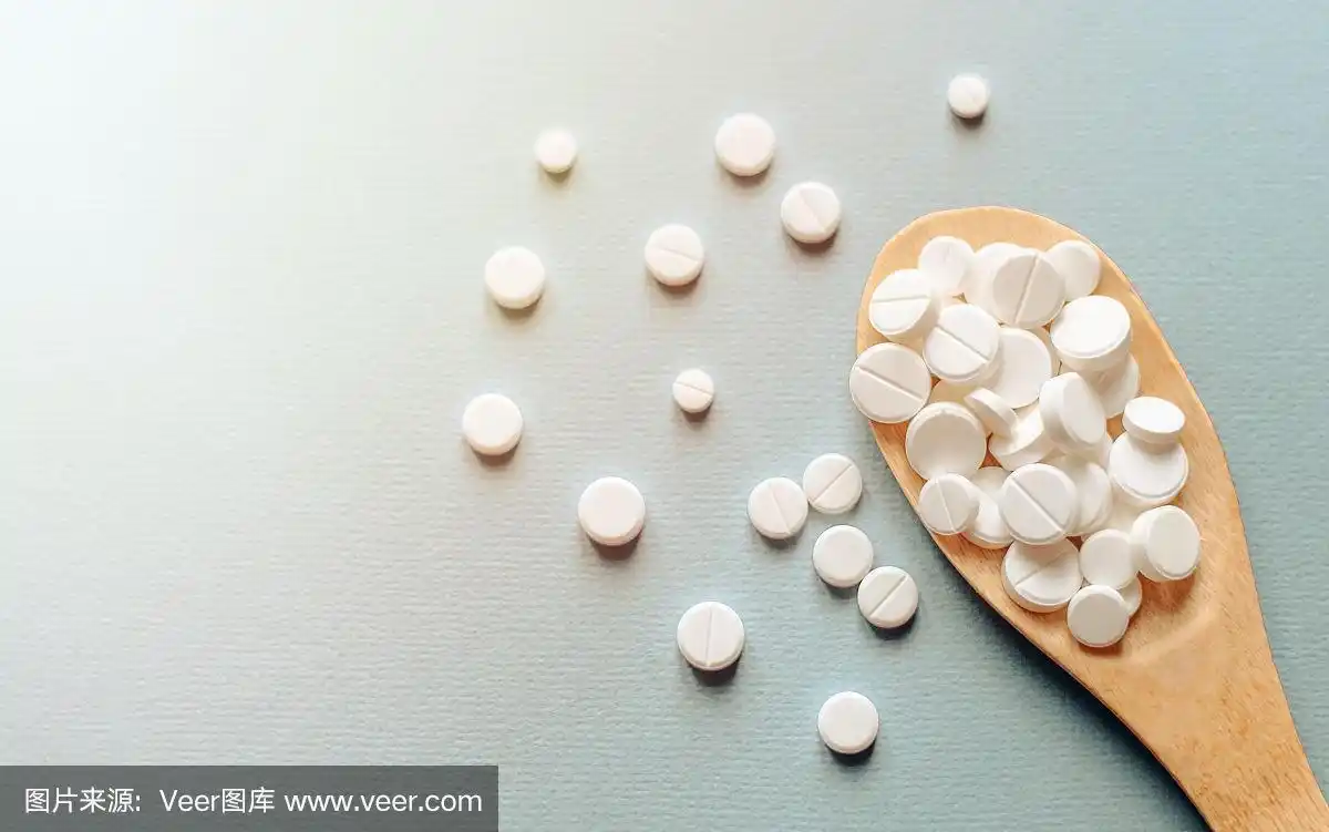 特写白色药片,药片在木勺里放在蓝色的桌子上,在阳光的照射下.医学健
