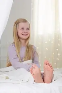 快乐的孩子女孩正坐在床上光着脚小孩子们坐在水中的木码头上, 享受着