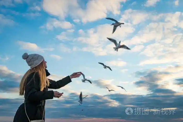 戴着白色的针织帽,在蓝天的映衬下,喂养着海滩上的海鸥