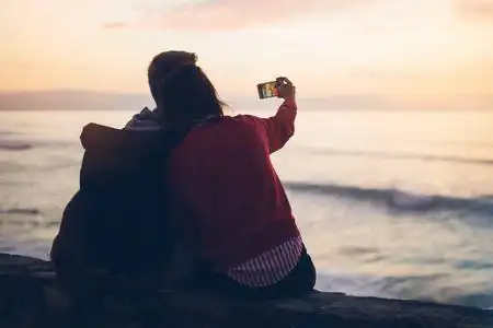 假期日出情侣在海滩上拥抱日出, 在移动智能手机上拍照, 两个浪漫的人