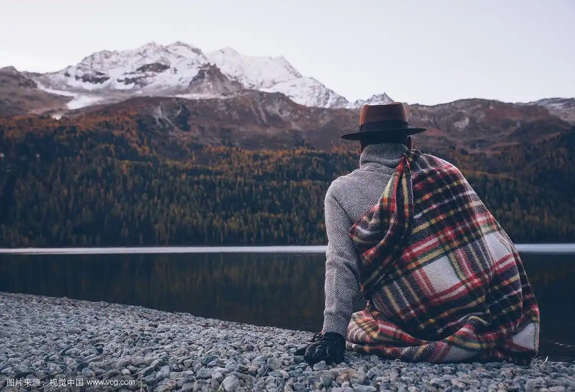 一个孤独的男人背着山在湖边的沙滩上欣赏日出