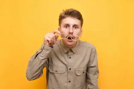 令人目瞪口呆黄色背景上惊讶的书呆子的肖像,摘下眼镜,带着震惊的脸