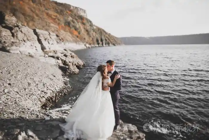 婚礼情侣接吻和拥抱蓝色海边的岩石上