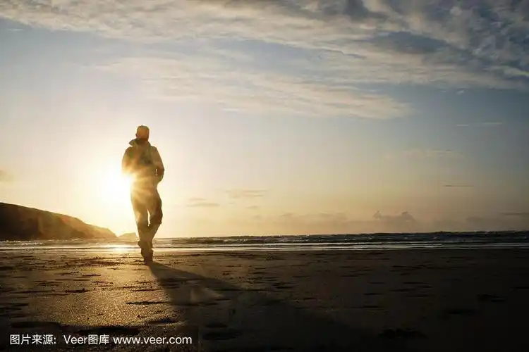 一个背影照亮的人漫步在fistral海滩,纽基,康沃尔在金色的秋天日落