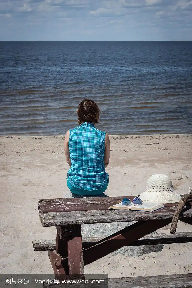 一个女人坐在海滩上的野餐桌上看着大海