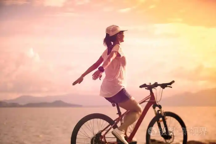 年轻女子骑自行车在阳光明媚的海滨, 伸出双臂