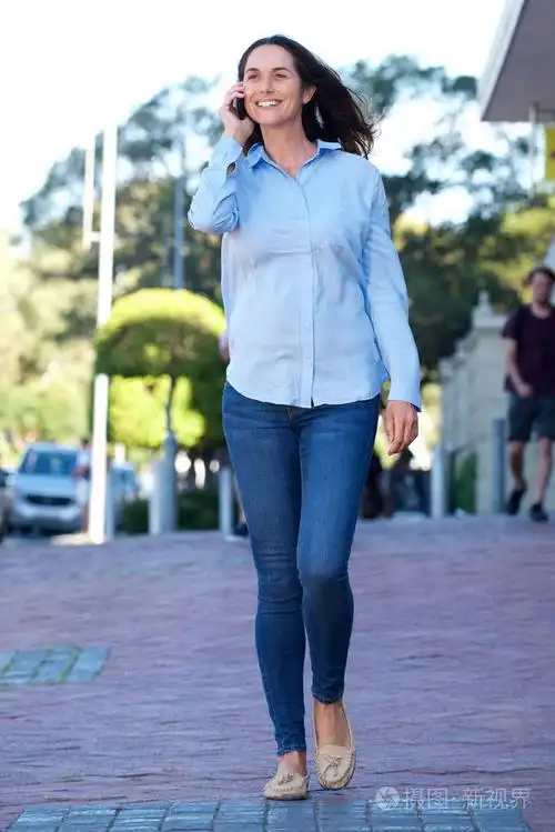 微笑的老妇人的全身肖像走路和交谈与移动电话