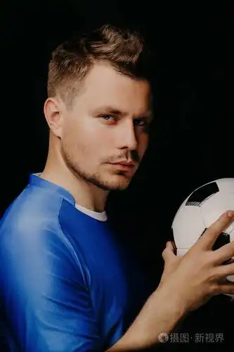 年轻英俊足球运动员的特写肖像在黑暗背景下摆出的足球