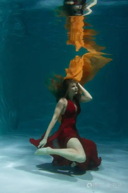 一个美丽的自由潜水员,一个人穿着红色的长裙,独自在深水中游泳