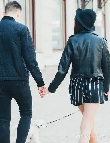 一对年轻的夫妇在黑色夹克, 手, 机智的背面视图