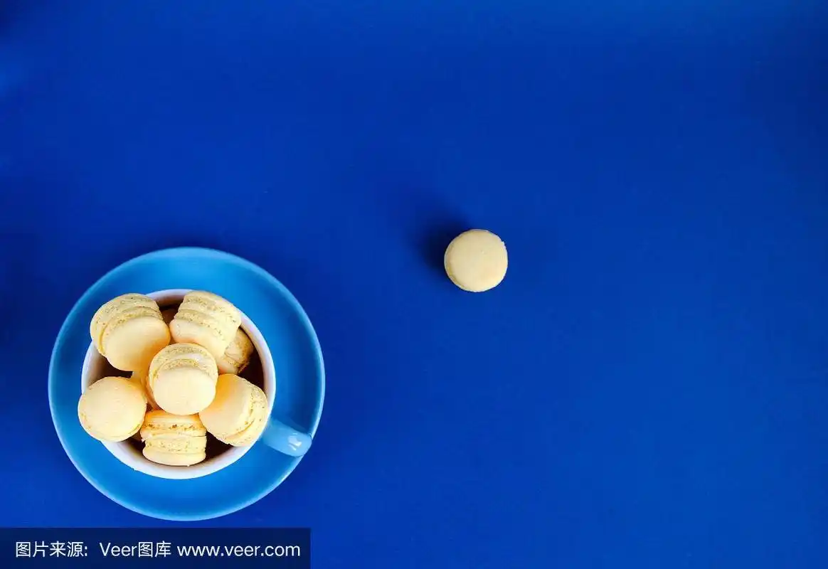 马卡龙在蓝色的杯子上,蓝色的背景,颜色趋势是2020,杯子的趋势是在