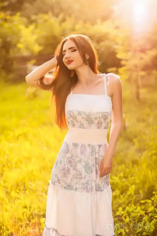 阳光明媚的田野上美丽的年轻女子.吹长的红头发.夏天.阳光明媚背光.