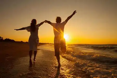 快乐的情侣在沙滩上奔跑照片