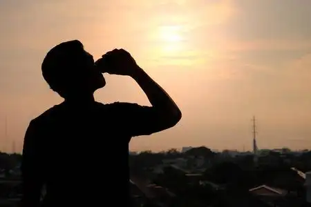 喝剪影一个男人在夕阳背景下喝着提神啤酒的剪影照片