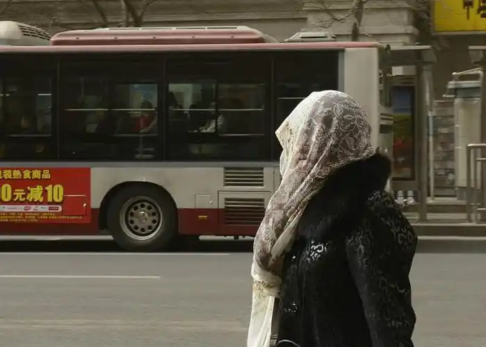 一名出行的市民用纱巾将头部紧紧包住,躲避沙尘,街头市民的纱巾被大风