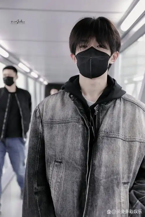 易烊千玺机场生图,他穿着渐变黑色牛仔外套,戴着黑色口罩,看起来帅气