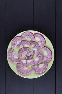 紫洋葱紫弓在一个绿色的盘子上, 洋葱在一个黑色的木质背景上, 洋葱片