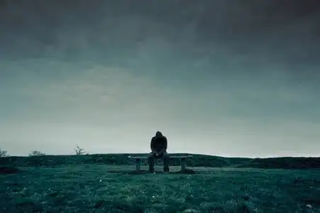 孤独身影一个孤独的戴着兜帽的身影坐在公园的长凳上,看上去悲伤,孤独