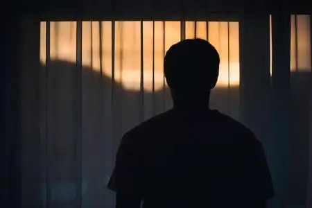 站在窗帘前, 望着窗外的哀伤的人的背部视图照片