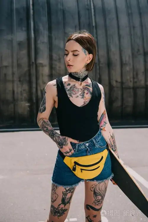 年轻迷人的纹身女孩手在口袋里拿着滑板在街上