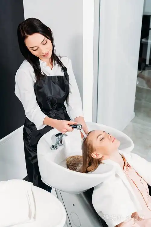 有吸引力的理发师洗头发为顾客在沙龙