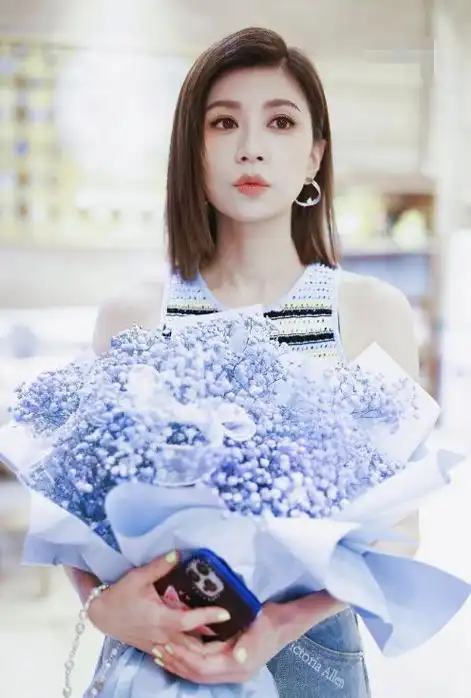 贾静雯手捧一束漂亮的鲜花,还留着迷人的长发,戴着银色的耳坠,感觉是