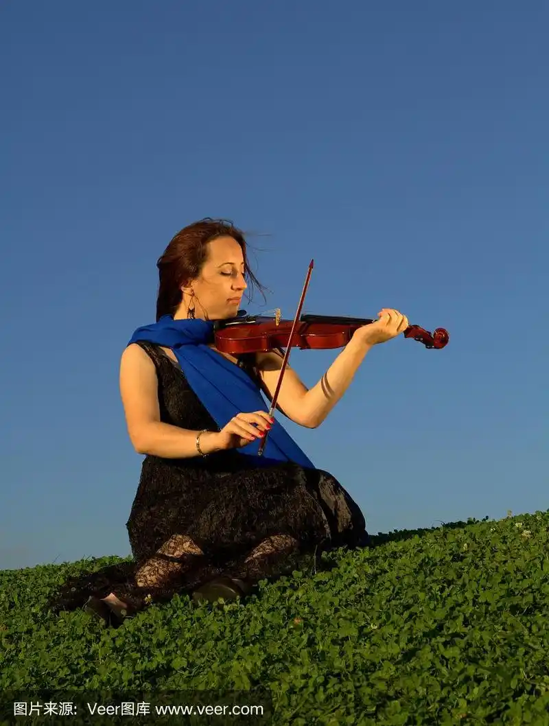 年轻女子坐在草地上拉小提琴