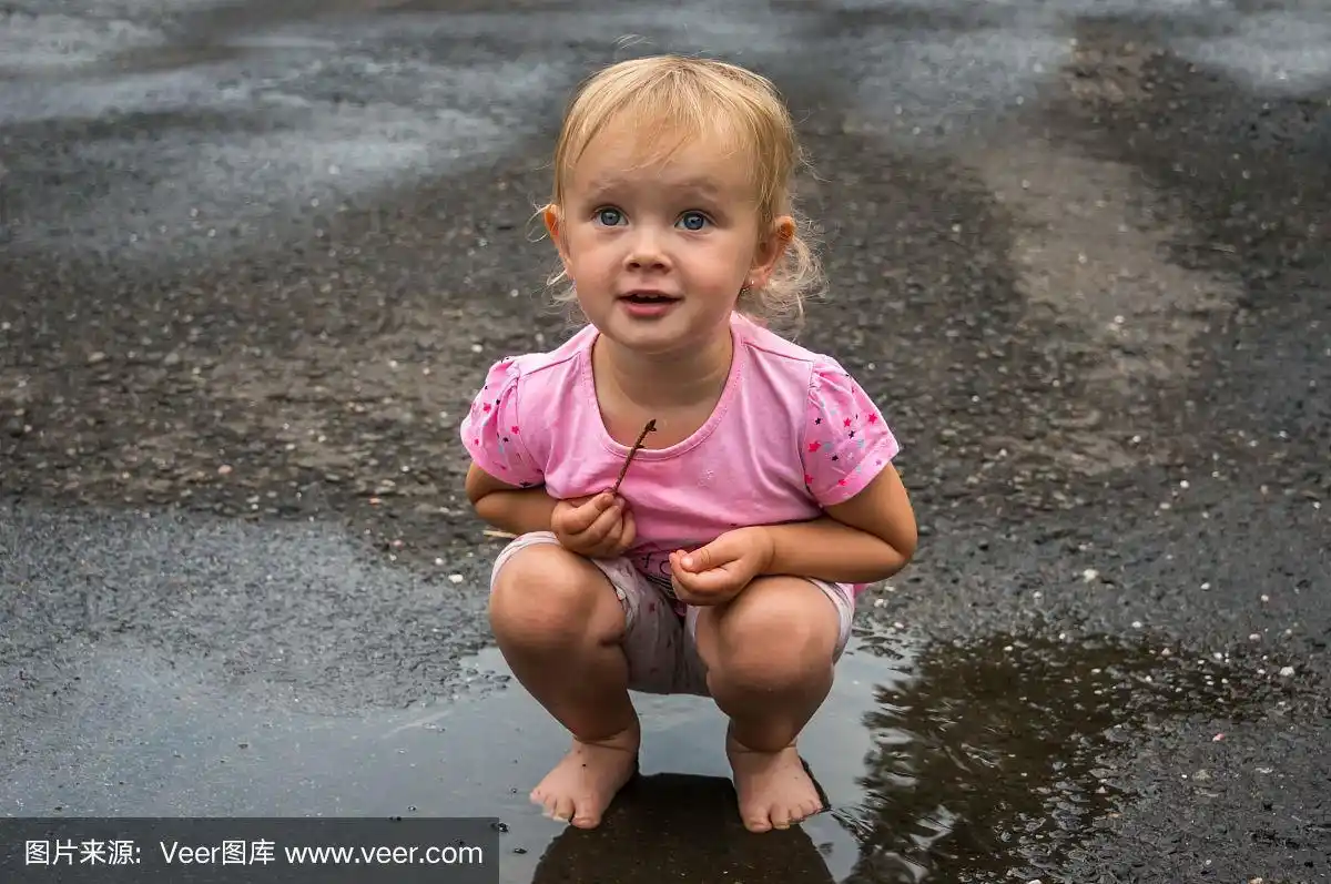 雨后,可爱的小女孩光着脚站在水坑里