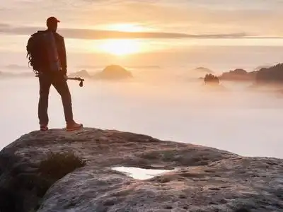 累运动累的徒步旅行者运动背包上岩石峰值和观看到深雾谷波纹管照片