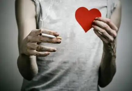 吸烟者手里拿着香烟,在黑暗的背景上有一颗红色的心照片