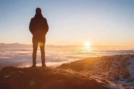 一个孤独的站在山上的人看着落日和日落的地平线,山谷里布满了云.