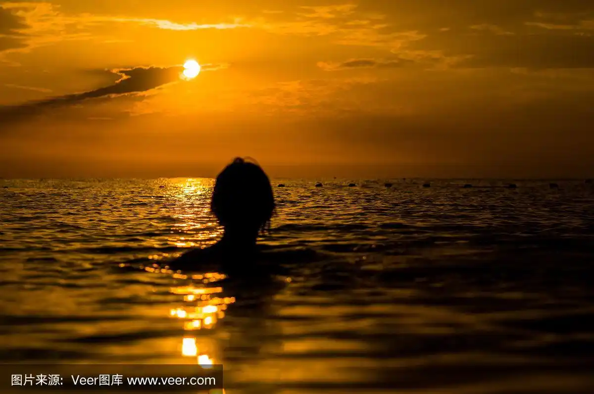 女孩在夕阳下的大海里游泳,水花透明,女性黑色的剪影