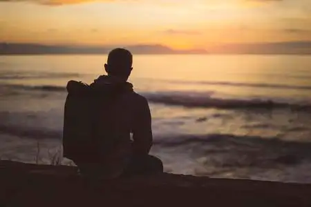 hipster徒步旅行者带背包,看着壮观的海景日落,背景蓝色的大海,享受