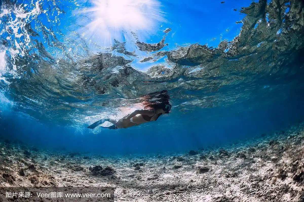 自由潜水的女人带着鳍在蓝色海洋的珊瑚上滑行.