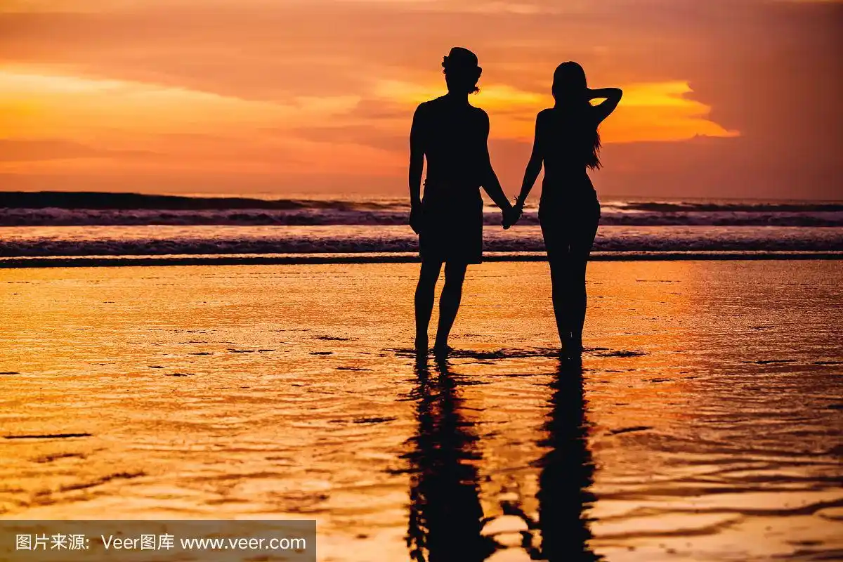 年轻情侣的剪影躺在海滩上
