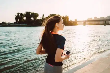 穿着运动服的长发少女在阳光下沿河奔跑照片